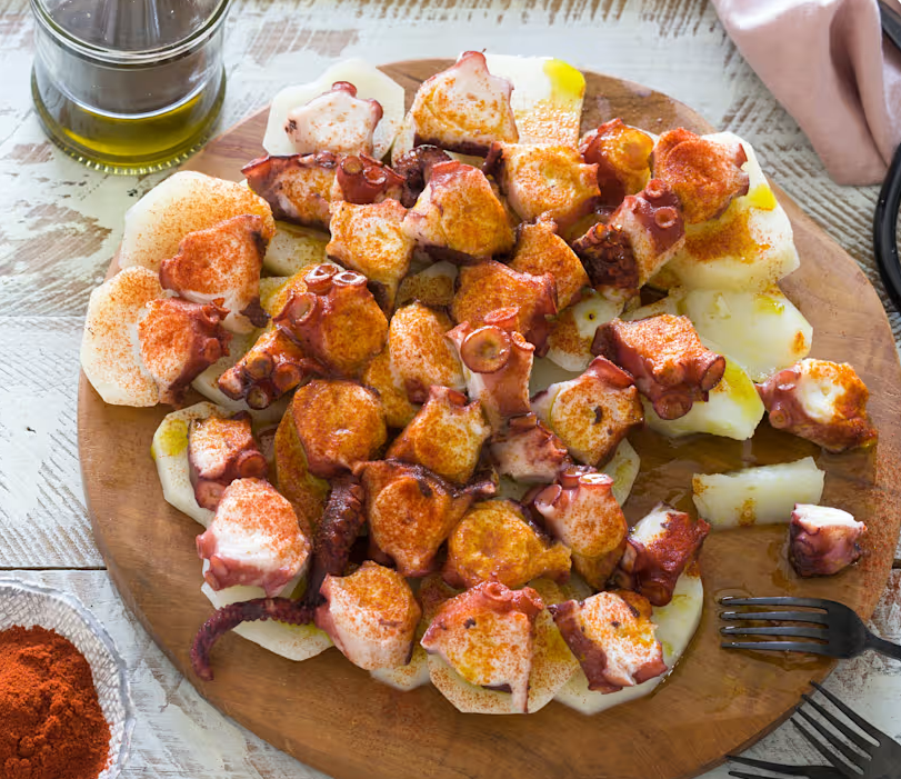 Pulpo á feira servido en plato de madera con pimentón, aceite de oliva y patatas - plato típico de Galicia, España